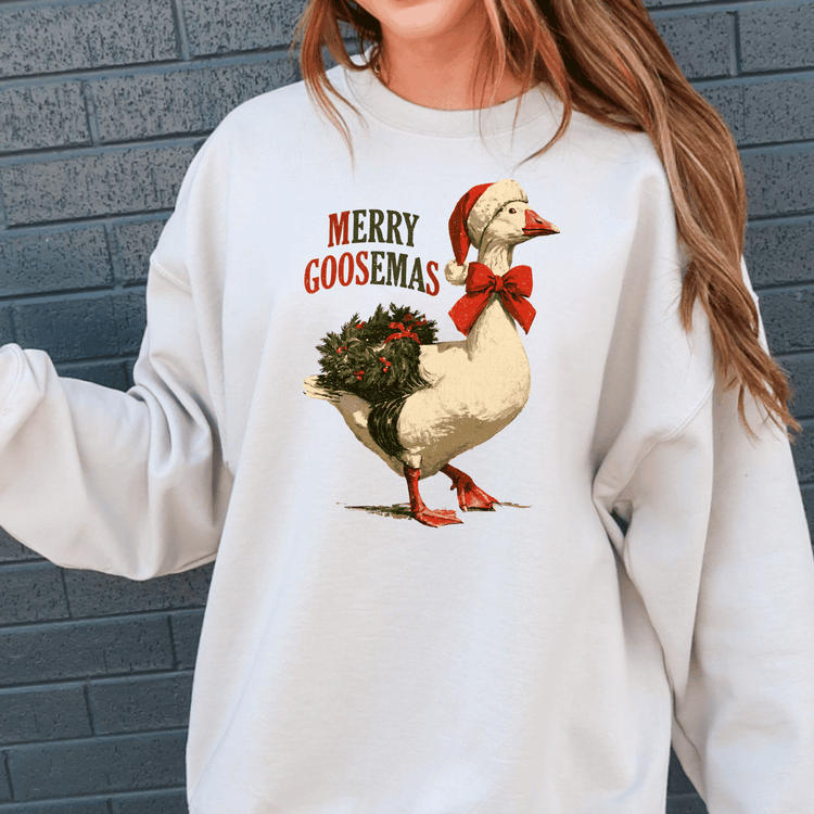 A white sweatshirt with a graphic of a goose wearing a Santa hat and carrying a Christmas wreath.