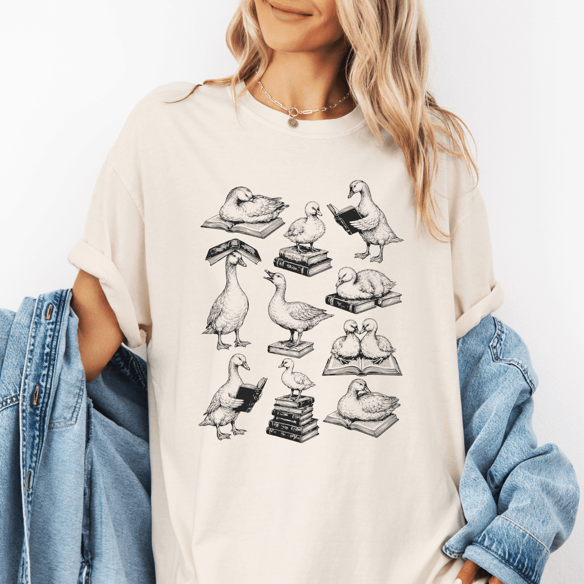 A woman wearing a white t-shirt with a graphic design of ducks reading books.