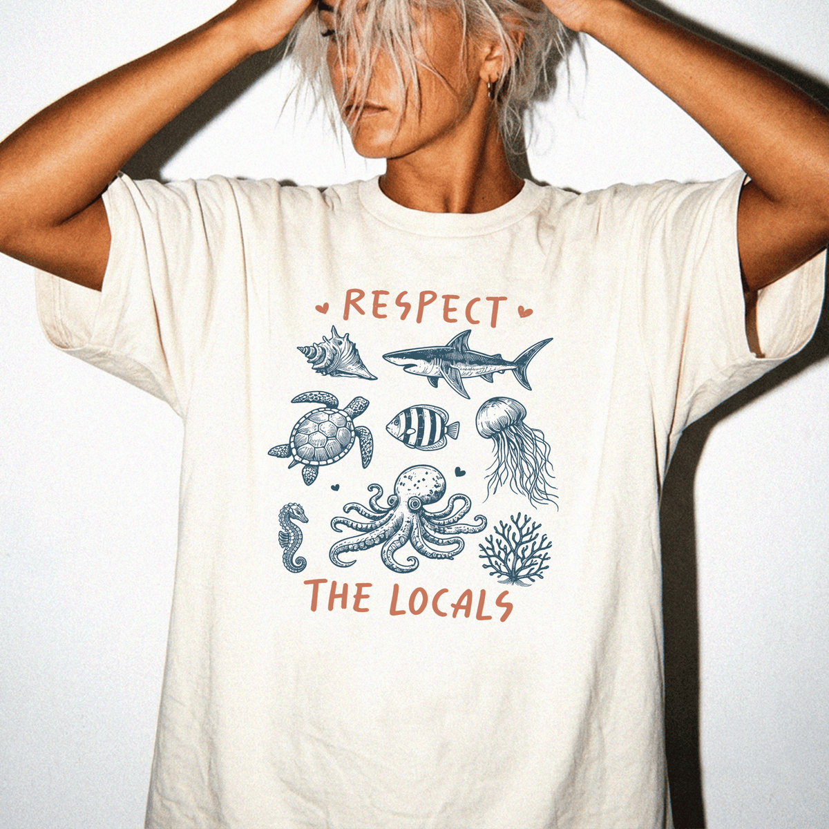 A person wearing a white t-shirt with a graphic design featuring various marine life, including a shark, turtle, fish, jellyfish, and coral, along with the text "RESPECT THE LOCALS".