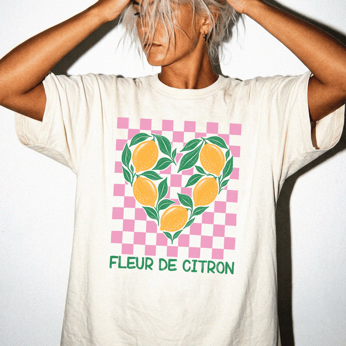 A person wearing a white t-shirt with a heart-shaped design featuring lemons and leaves, along with the text "FLEUR DE CITRON" printed on it.