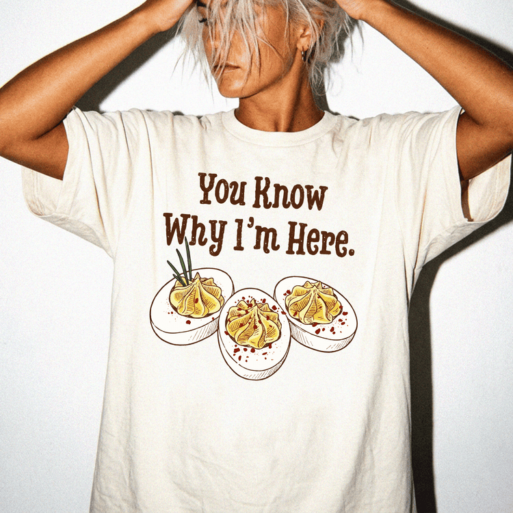 A person wearing a white t-shirt with a graphic design of three egg dishes and the text "You Know Why I'm Here."
