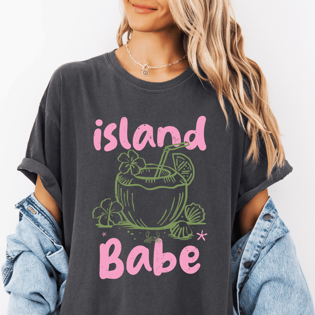 A woman wearing a gray t-shirt with a graphic design of a tropical drink and the text "island Babe" printed on it.