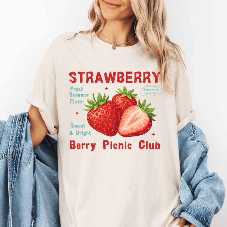 A woman wearing a white t-shirt with a graphic design of strawberries and text promoting a berry picnic club.