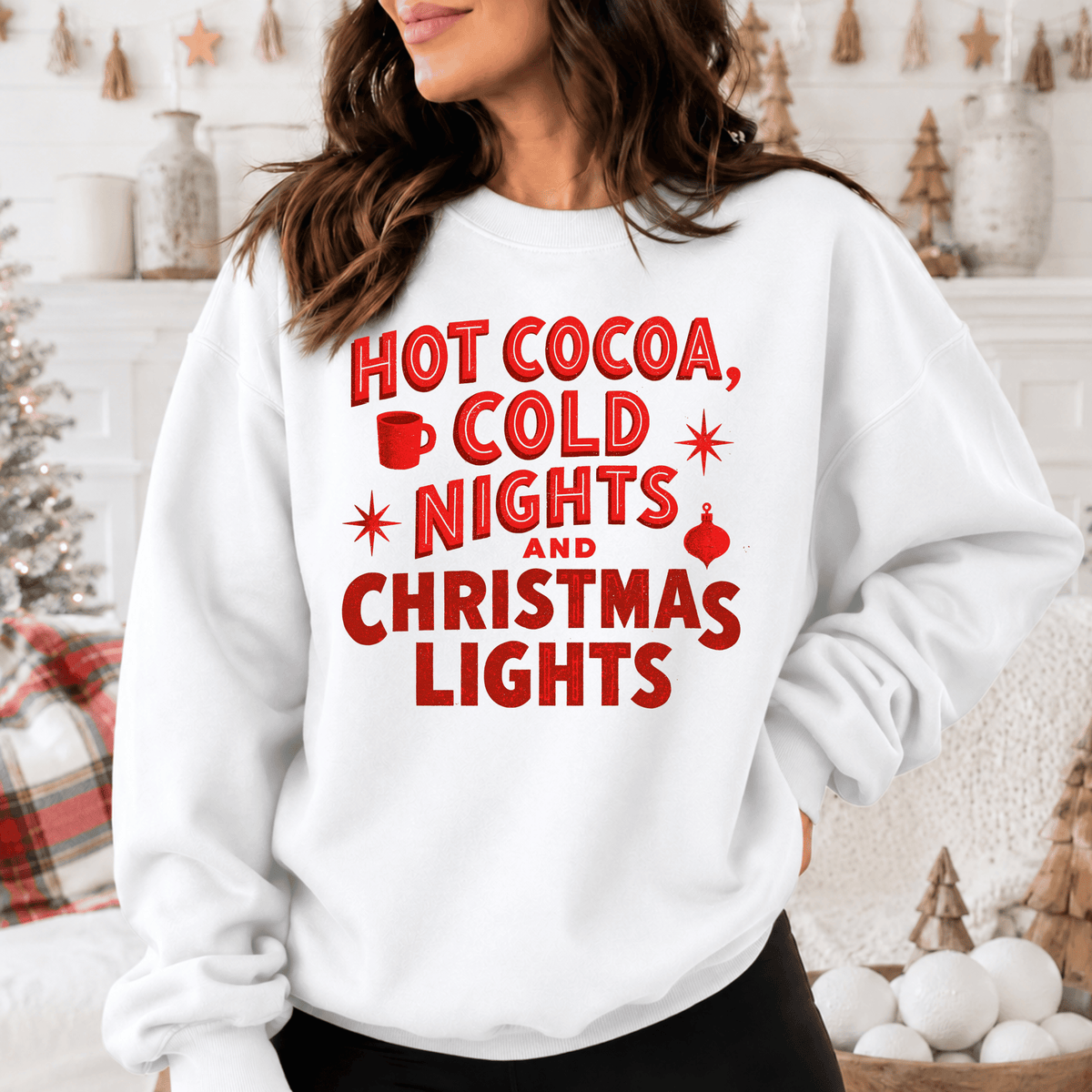 A woman wearing a white sweatshirt with red text that says "HOT COCOA, COLD NIGHTS AND CHRISTMAS LIGHTS".