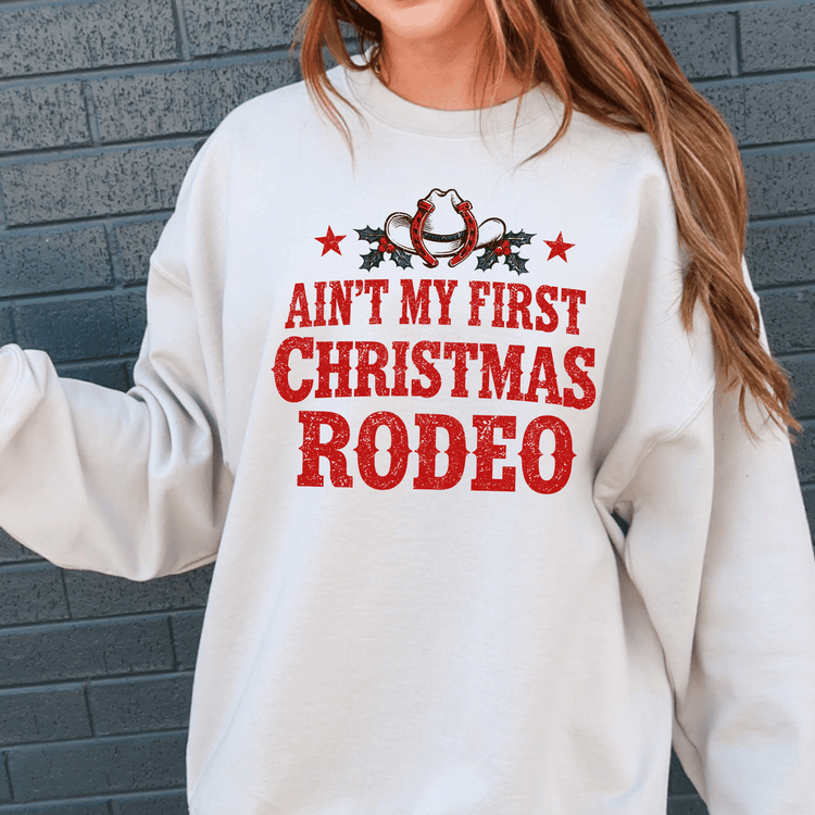 A woman wearing a white sweatshirt with a red and white graphic design that says "Ain't my first Christmas rodeo".