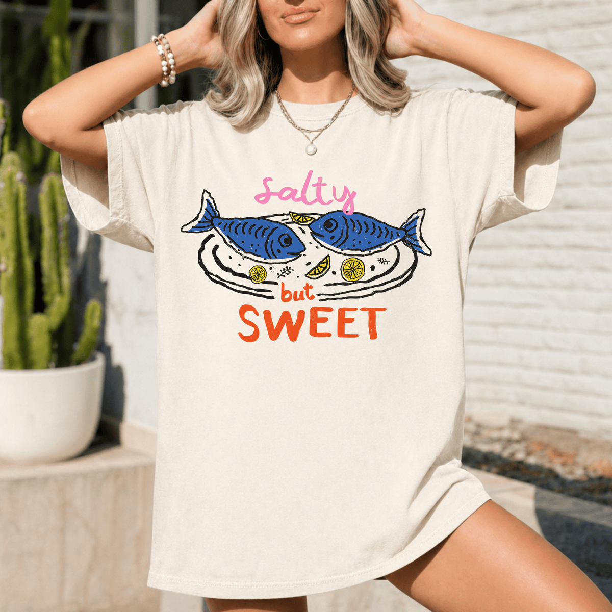 A woman wearing a white t-shirt with a graphic design of two fish and the text "Salty but Sweet" printed on it.