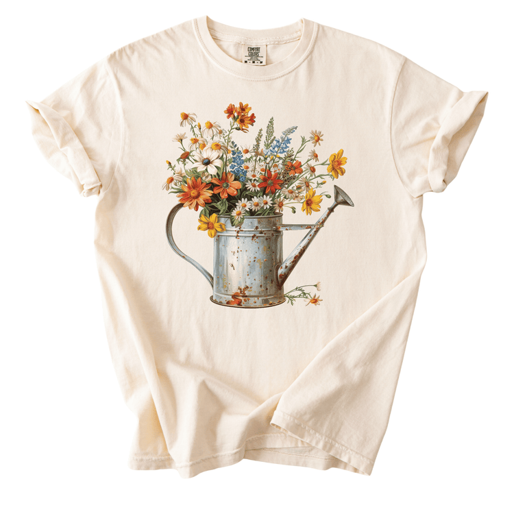 A white t-shirt with a printed image of a watering can filled with colorful flowers.