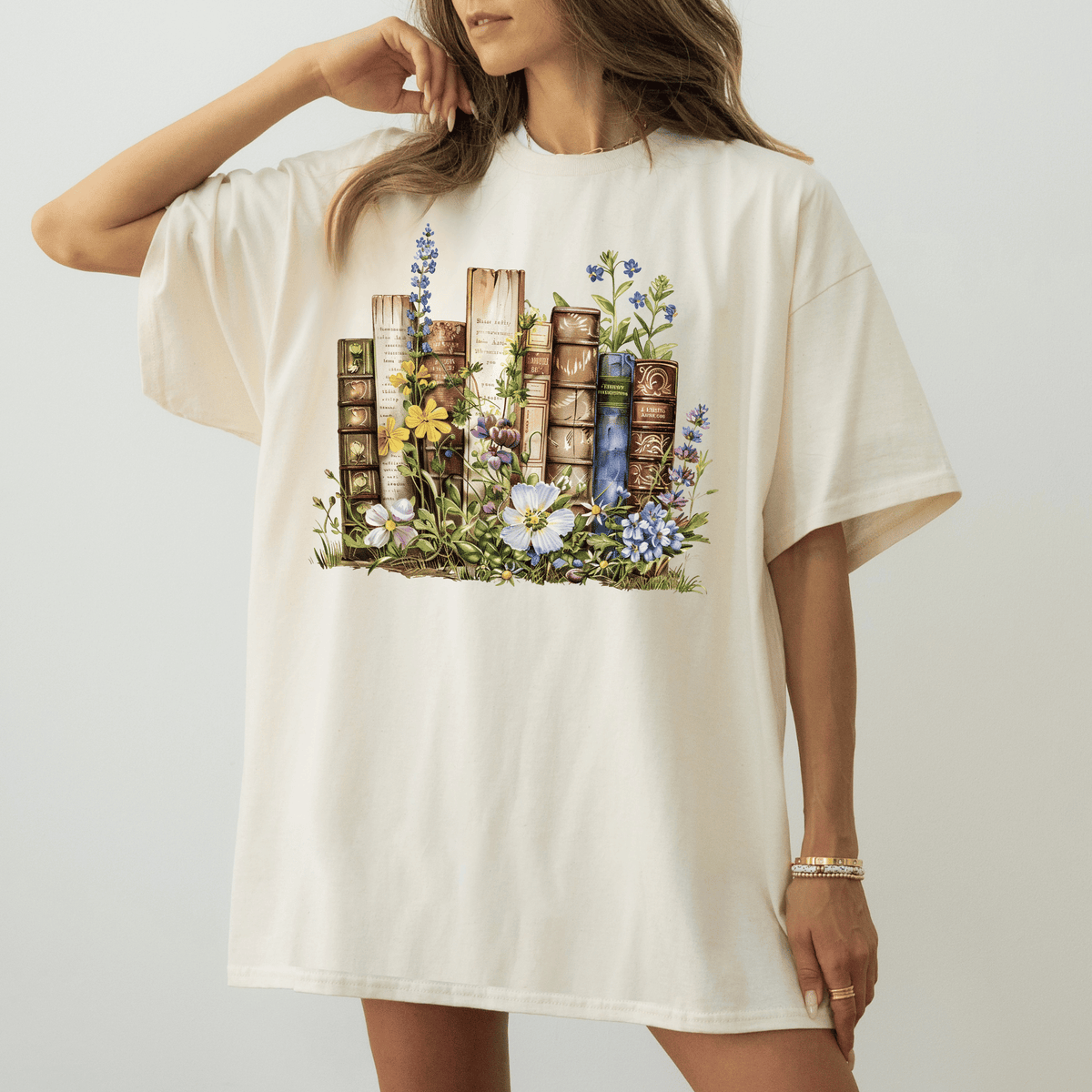 A woman wearing a white t-shirt with a printed design of books surrounded by flowers and plants.