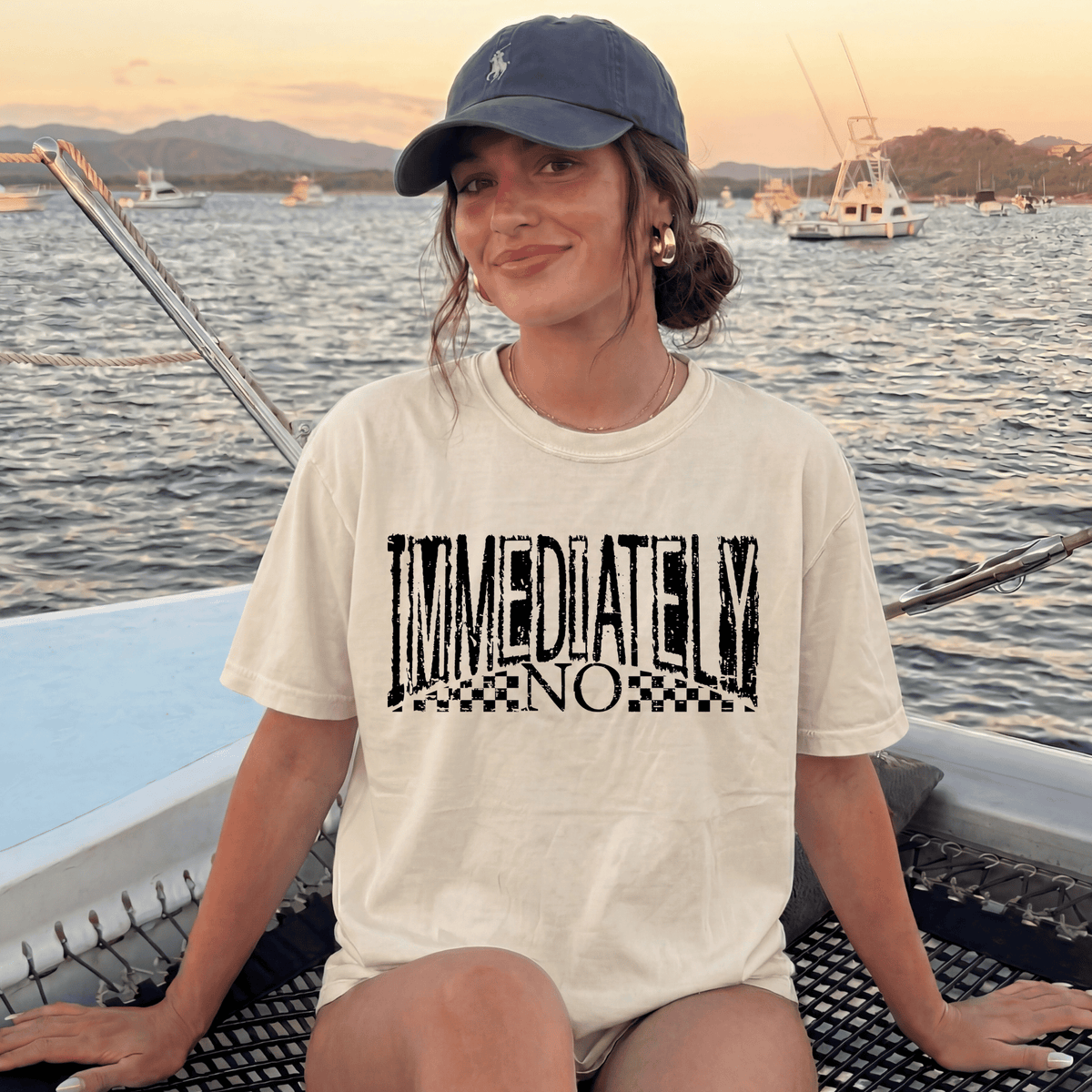 A woman wearing a white t-shirt with the text "IMMEDIATELY NO" is sitting on a boat, smiling at the camera.