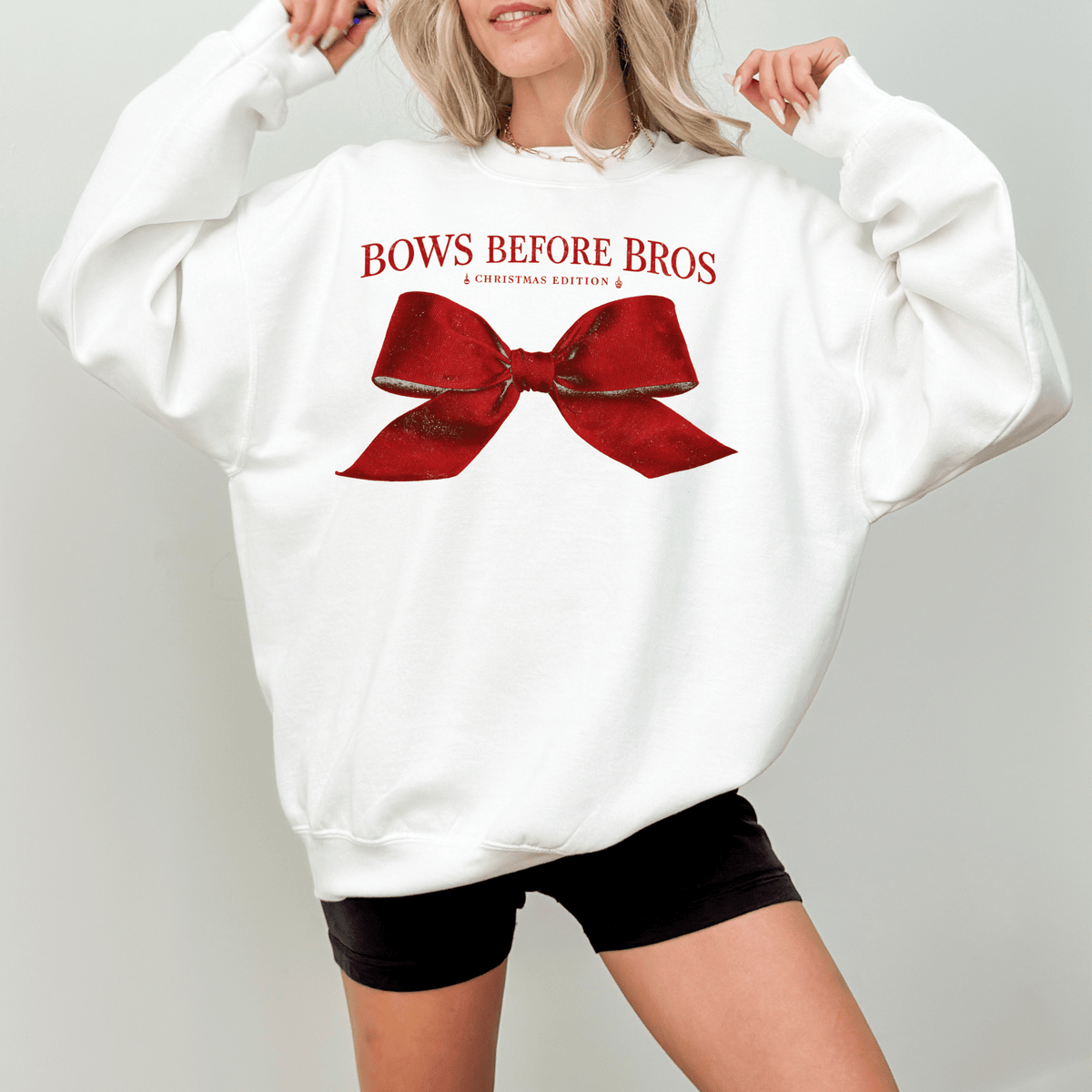 A woman wearing a white sweatshirt with a red bow and the text "BOWS BEFORE BROS" printed on it.