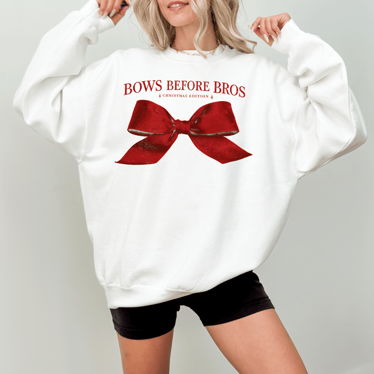 A woman wearing a white sweatshirt with a red bow and the text "BOWS BEFORE BROS" printed on it.