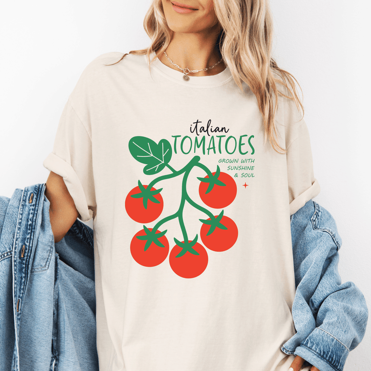 A woman wearing a white t-shirt with a graphic of tomatoes and text, standing next to a denim jacket.