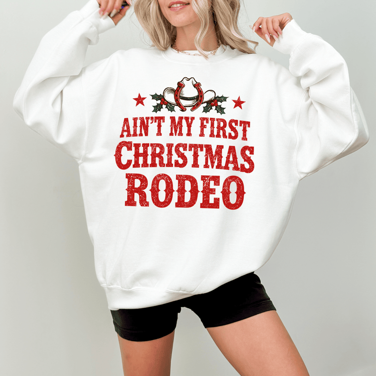 A woman wearing a white sweatshirt with a red and black graphic design that says "Ain't my first Christmas rodeo".