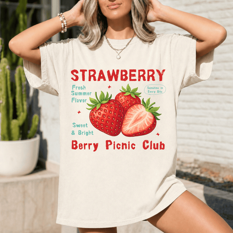 A woman wearing a white t-shirt with a graphic design of strawberries and text promoting a berry picnic club.