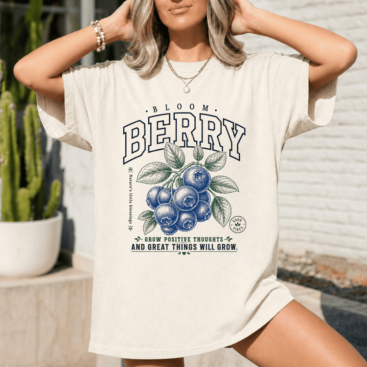 A woman wearing a white t-shirt with a graphic design of blueberries and leaves, along with the text "Bloom Berry" and "Grow positive thoughts - and great things will grow."