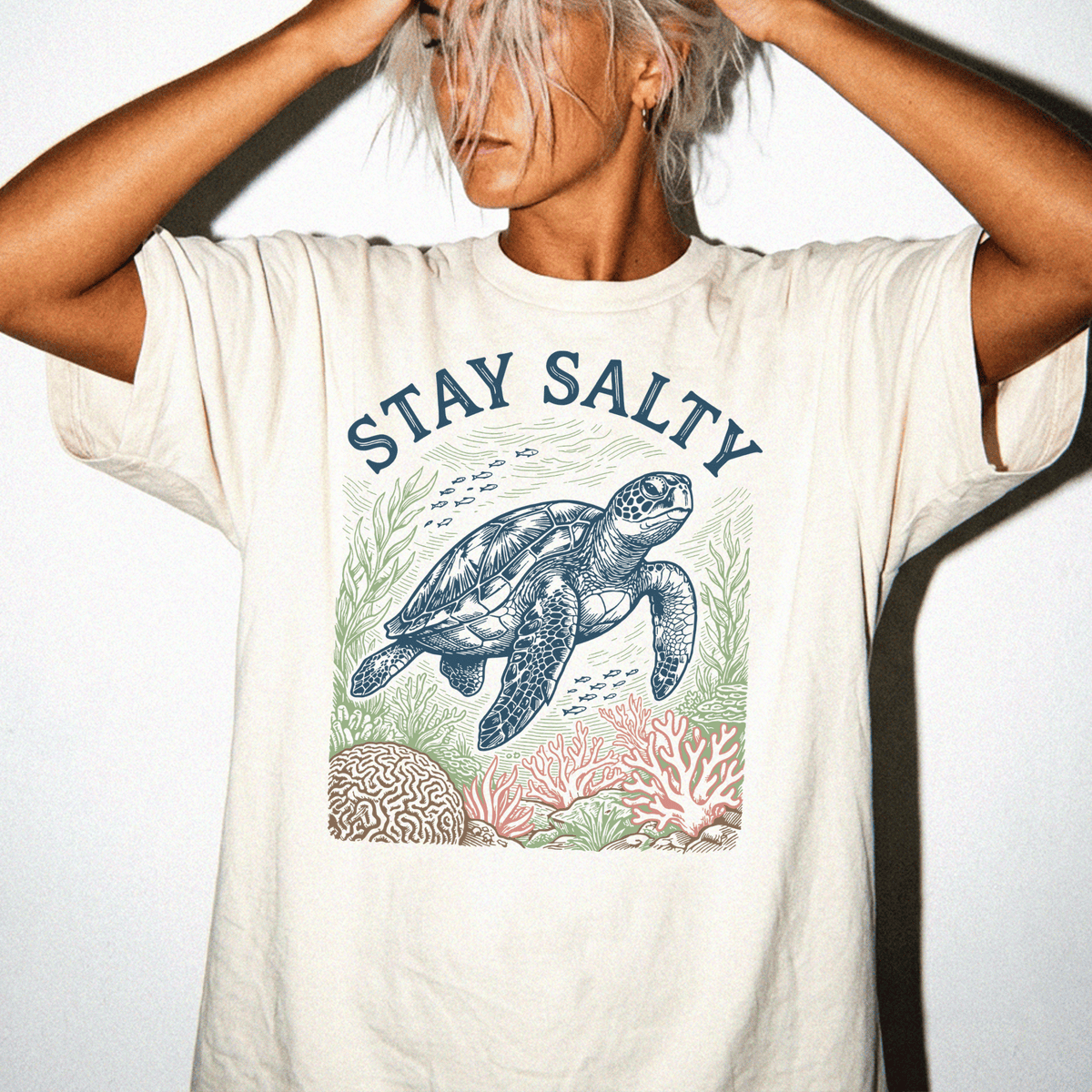 A person wearing a white t-shirt with a graphic design of a sea turtle and coral reef.