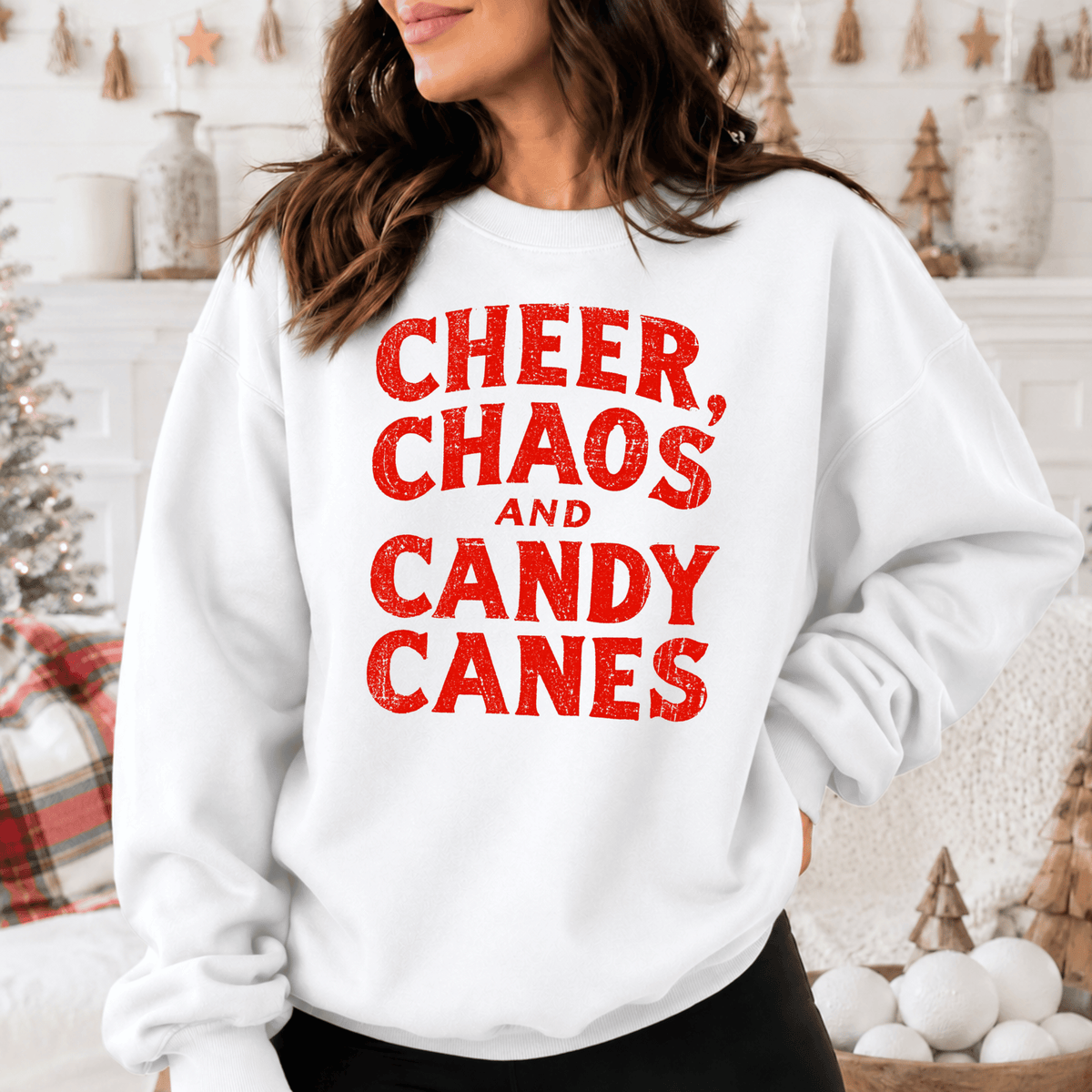 A woman wearing a white sweatshirt with the text "CHEER, CHAOS AND CANDY CANES" printed on it.