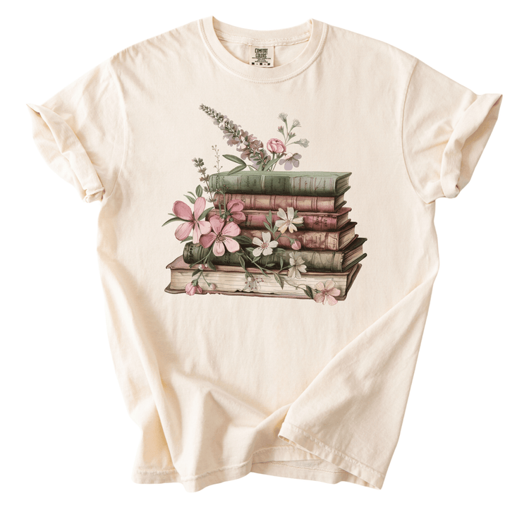 A white t-shirt with a printed design of a stack of books adorned with flowers.