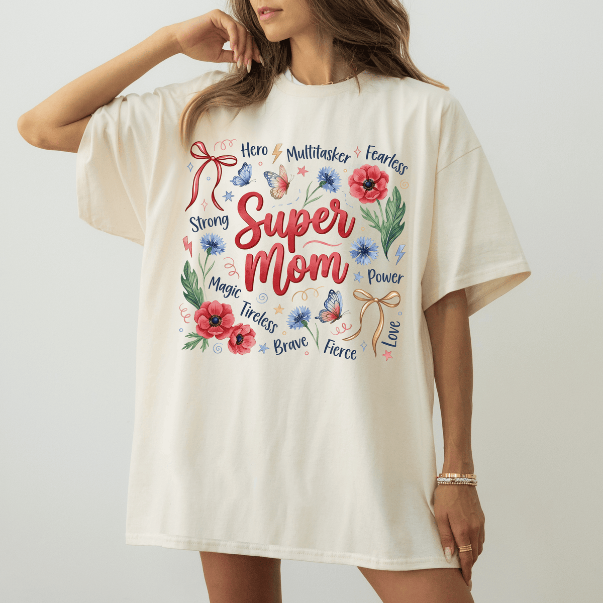 A woman wearing a white t-shirt with a colorful graphic design that says "Super Mom" surrounded by various words and illustrations.