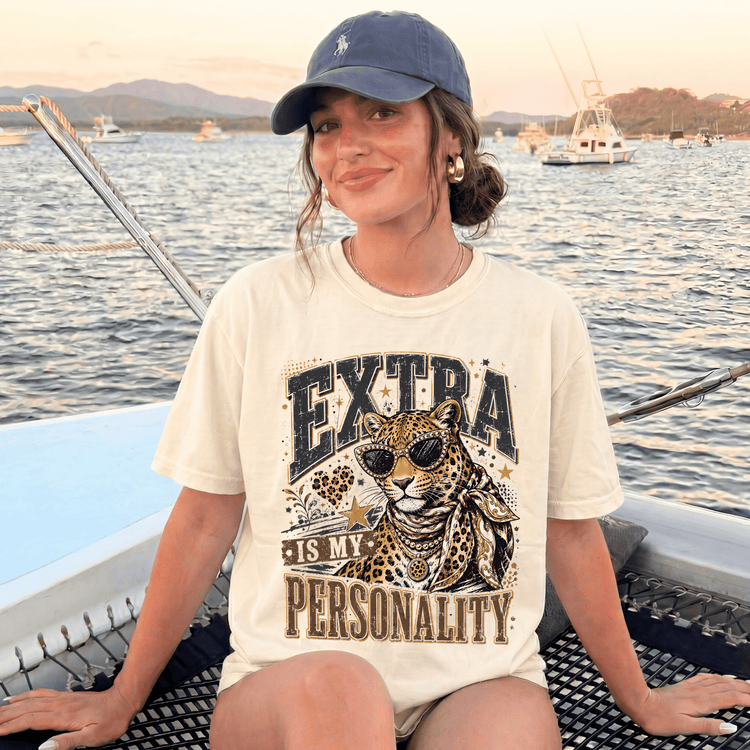 A woman wearing a white t-shirt with a leopard graphic and text, sitting on a boat in the water.