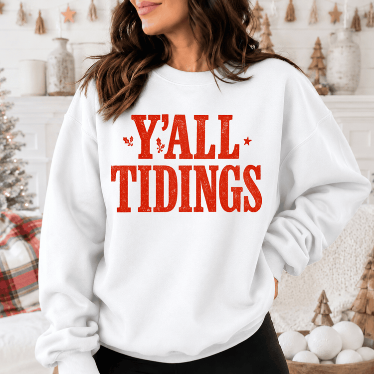 A woman wearing a white sweatshirt with the text "Y'ALL TIDINGS" printed on it.