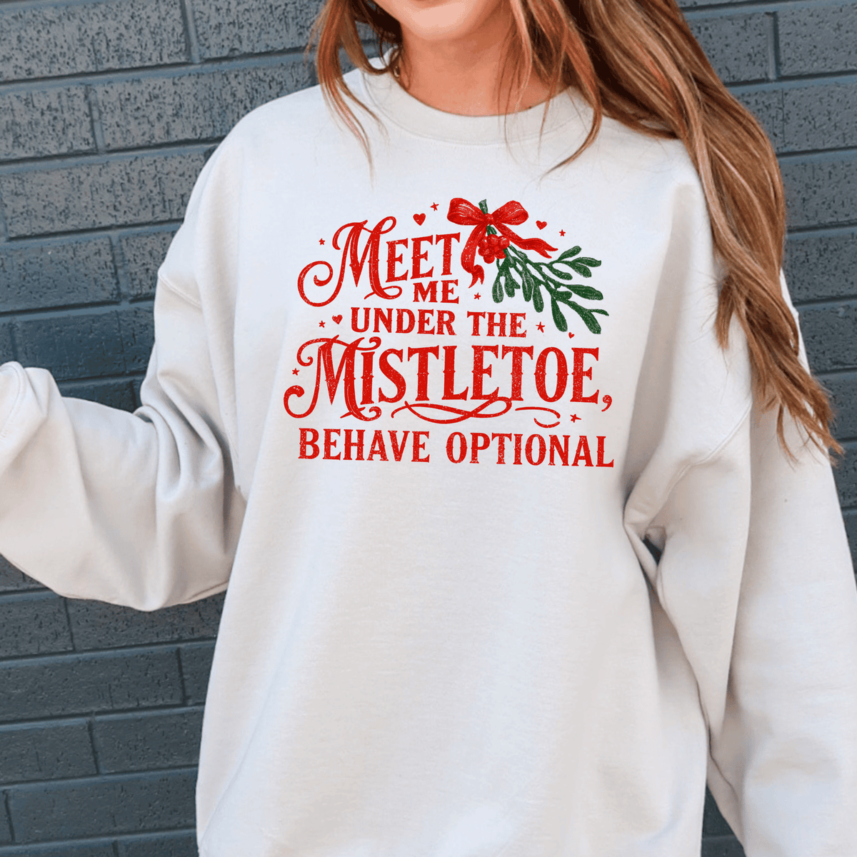 A white sweatshirt with a red and green text design that reads "Meet me under the mistletoe, behave optional".