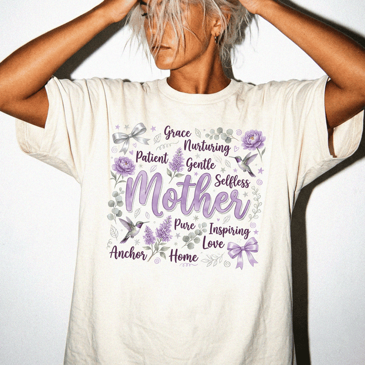 A woman wearing a white t-shirt with a graphic design featuring the words "Grace, Nurturing, Patient, Gentle, Selfless, Pure, Inspiring, Anchor, Home, Love" surrounded by purple flowers and birds.