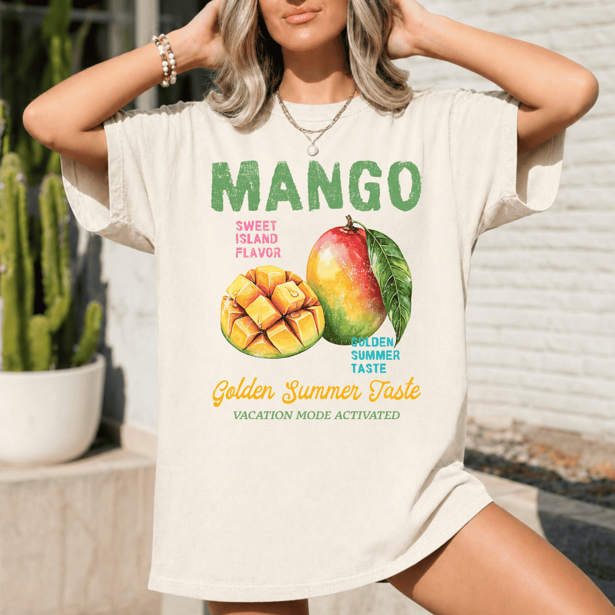 A woman wearing a white t-shirt with a graphic design featuring a mango and a pineapple, along with the text "Mango Sweet Island Flavor Golden Summer Taste Vacation Mode Activated".