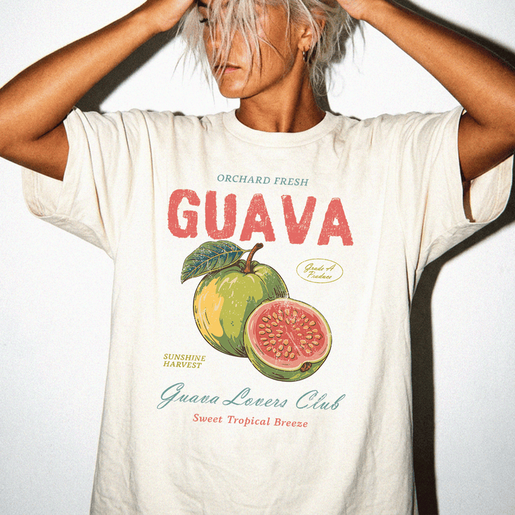 A person wearing a white t-shirt with a graphic design of a guava fruit and text that says "Orchard Fresh GUAVA" and "Guava Lovers Club Sweet Tropical Breeze".