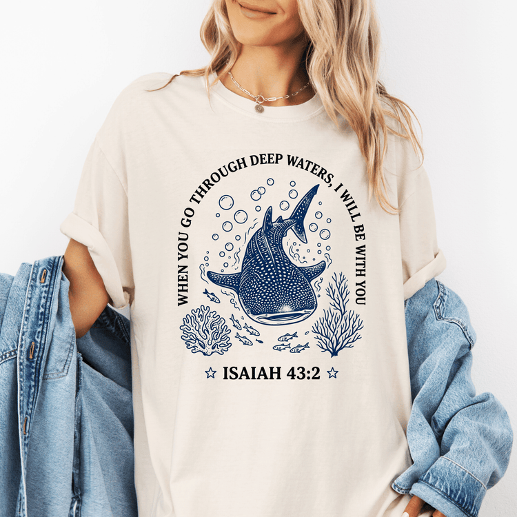 A woman wearing a white t-shirt with a graphic design featuring a blue whale surrounded by bubbles and marine life, along with the text " Isaiah 43:2" and a Bible verse reference.