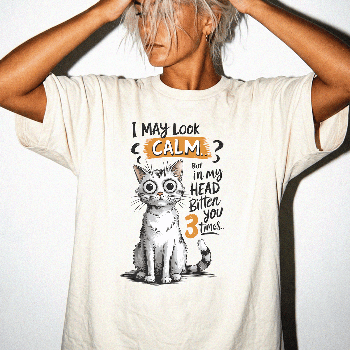 A person wearing a white t-shirt with a graphic of a cat and text that says "I may look calm, but in my head bitten you 3 times".