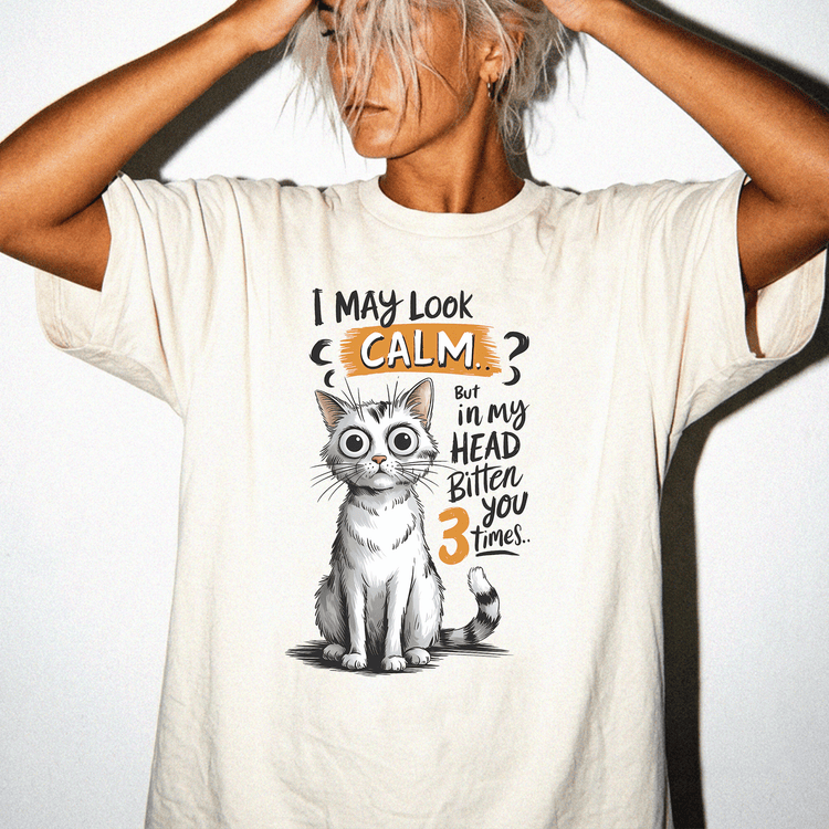 A person wearing a white t-shirt with a graphic of a cat and text that says "I may look calm, but in my head bitten you 3 times".
