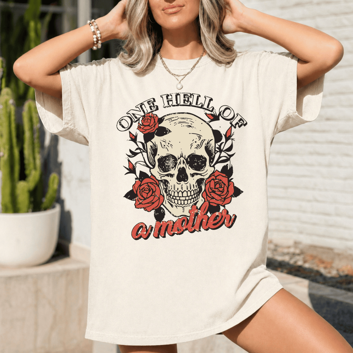 A woman wearing a white t-shirt with a skull design and the text "One Hell of a Mother" printed on it.