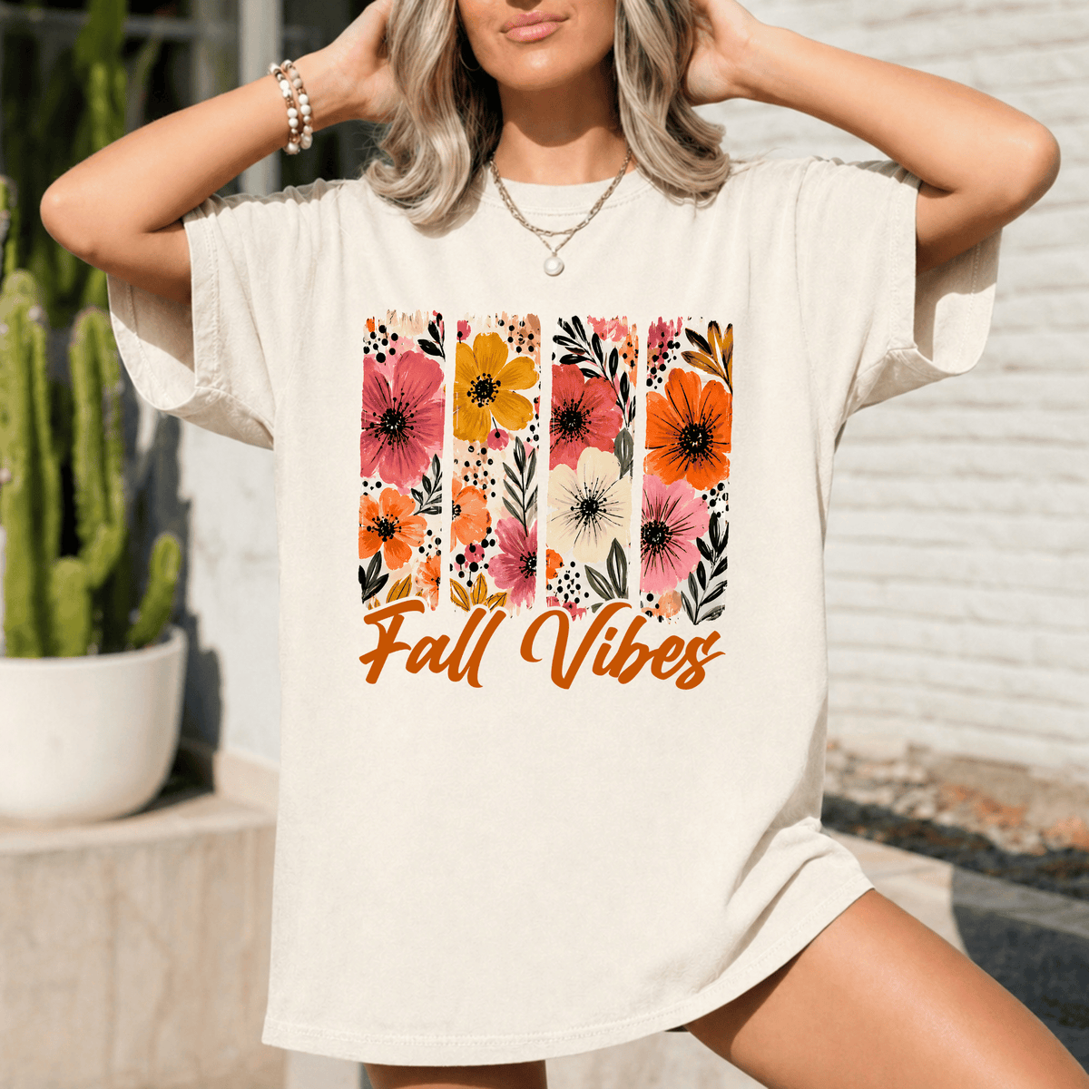 A woman wearing a white t-shirt with a floral design and the text "Fall Vibes" printed on it.