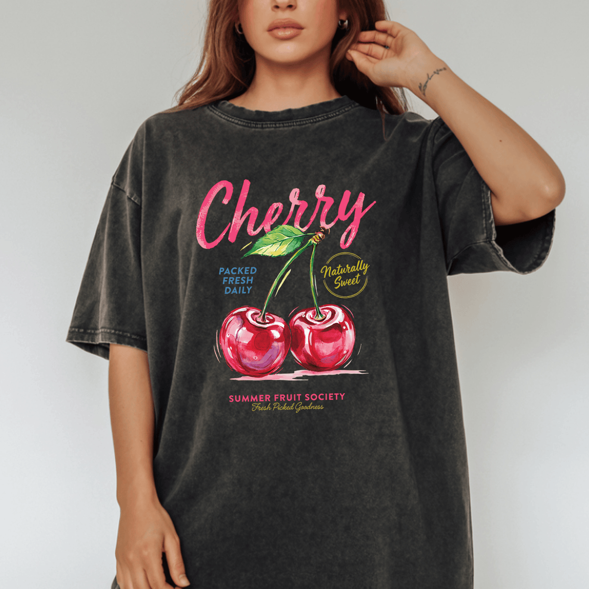 A woman wearing a black t-shirt with a graphic design of two cherries and text related to fruit.