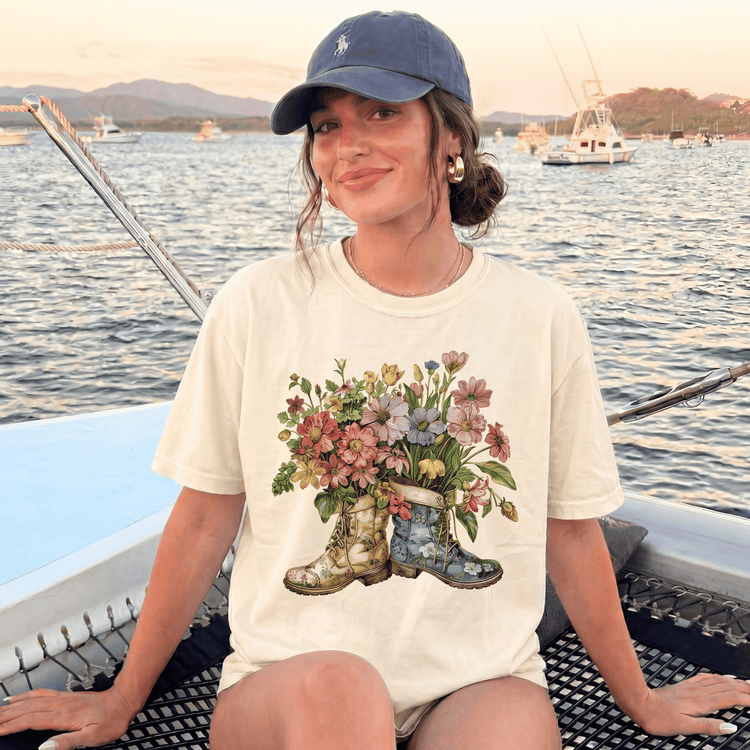 A woman wearing a white t-shirt with a floral design and a baseball cap is sitting on a boat, smiling at the camera.