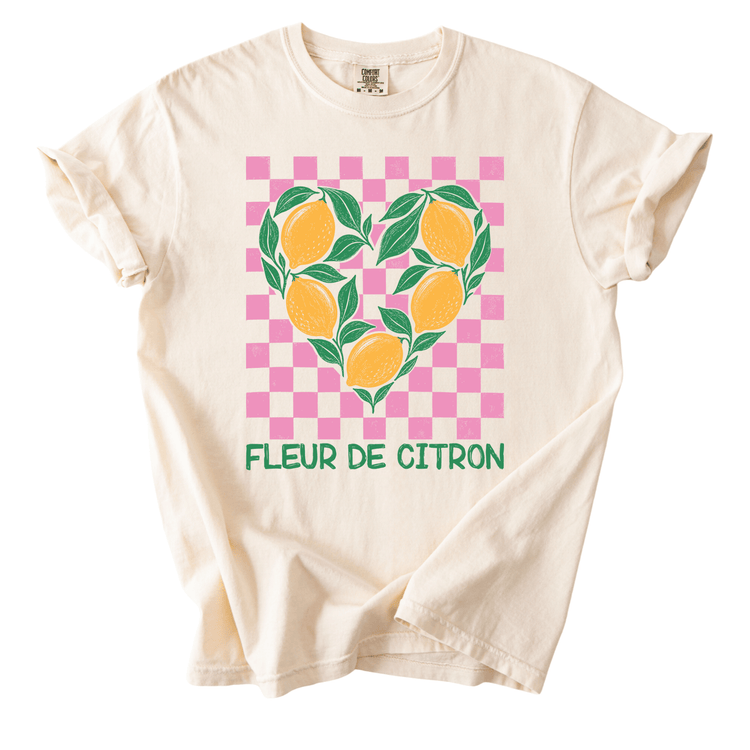 A white t-shirt with a graphic design featuring a heart shape made up of oranges and leaves, along with the text "Fleur de Citron" printed on it.