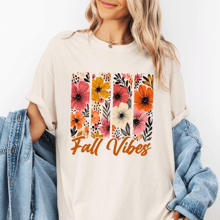 A woman wearing a white t-shirt with a floral design and the text "Fall Vibes" printed on it, along with a denim jacket.