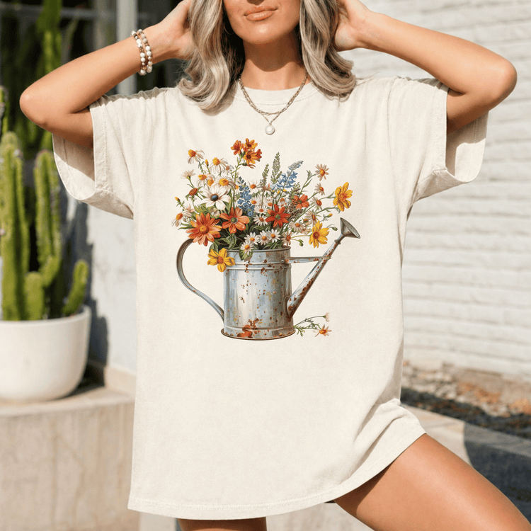 A woman wearing a white t-shirt with a printed image of a watering can filled with colorful flowers.
