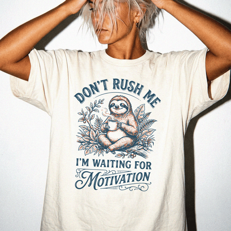 A person wearing a white t-shirt with a graphic design featuring a sloth and the text "Don't Rush Me I'm Waiting for Motivation".