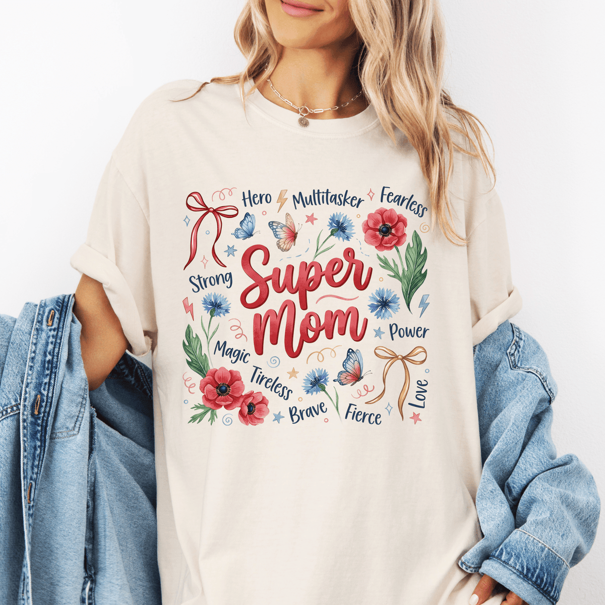 A woman wearing a white t-shirt with a graphic design featuring the words "Super Mom" surrounded by various flowers and butterflies.