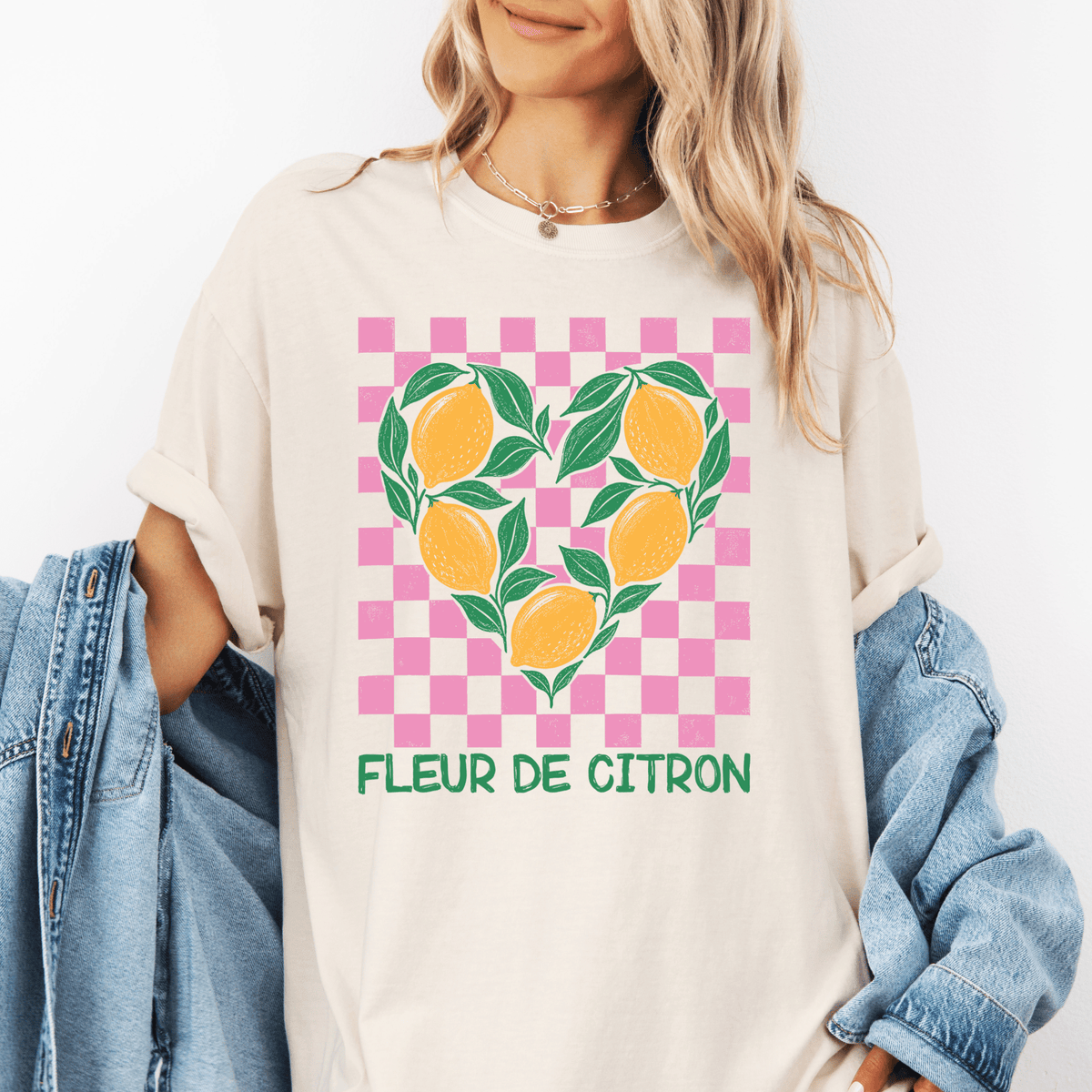 A woman wearing a white t-shirt with a graphic design of a heart made up of lemons and leaves, along with the text "Fleur de Citron" printed on it.