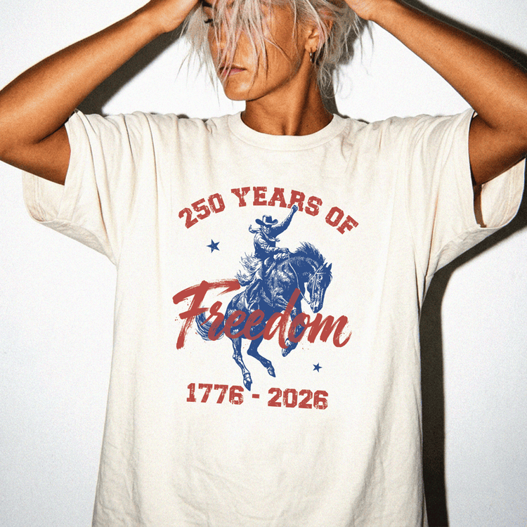 A person wearing a white t-shirt with a graphic design that says "250 YEARS OF Freedom" and "1776-2026".