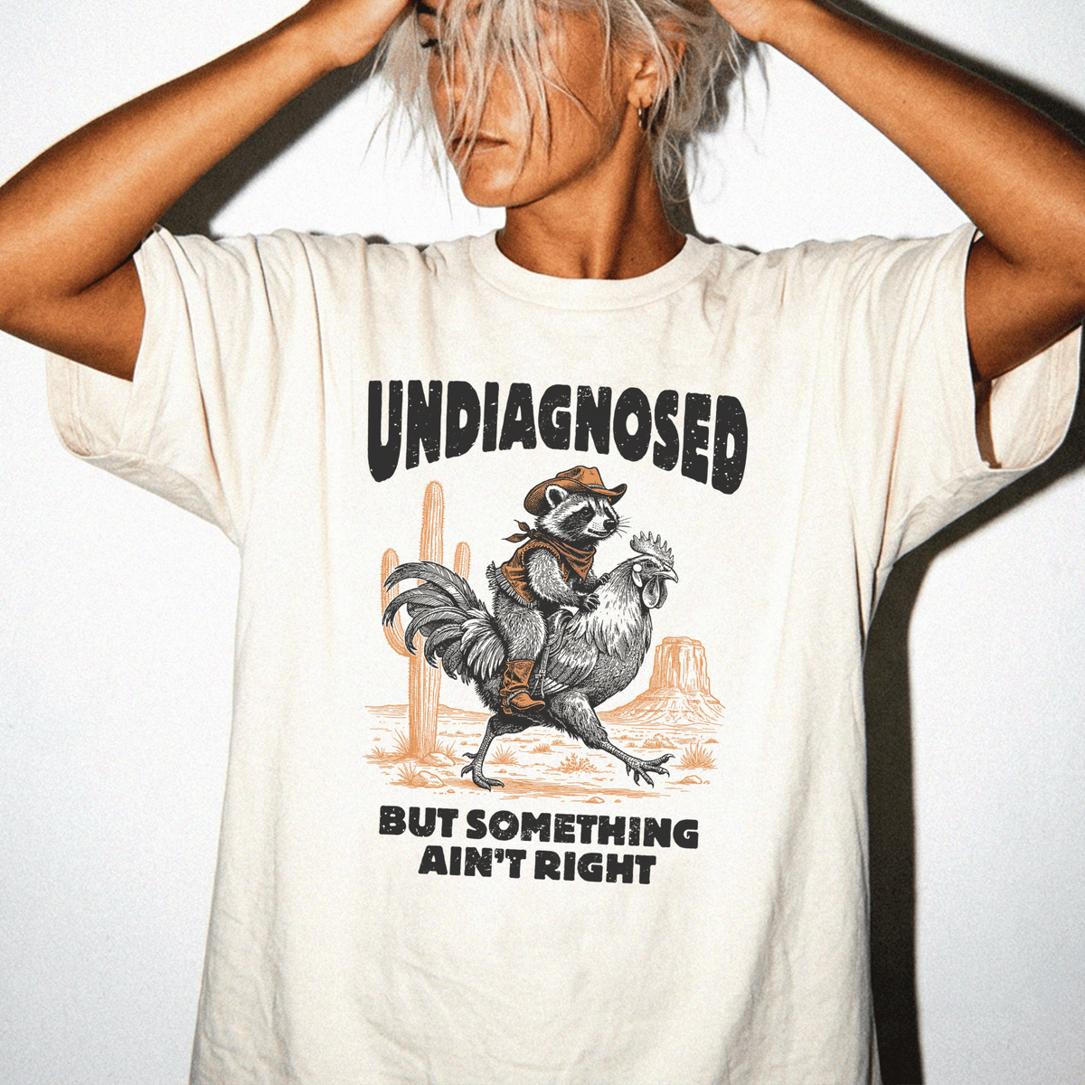 A person wearing a white t-shirt with a graphic design depicting a raccoon riding a rooster.