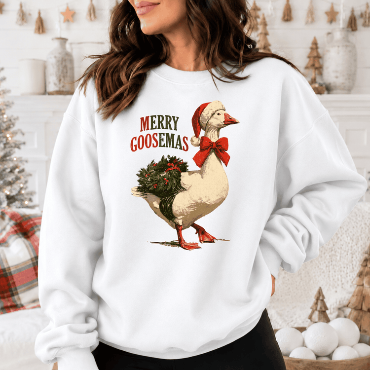 A woman wearing a white sweatshirt with a graphic of a goose wearing a Santa hat and a wreath on its back.