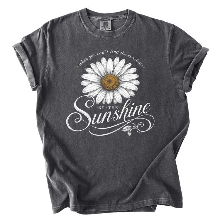 A gray t-shirt with a white daisy flower design and the text "Be the sunshine" printed on it.