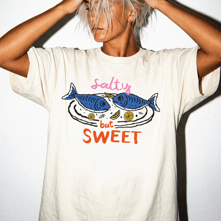 A person wearing a white t-shirt with a graphic design of two fish and the text "Salty but SWEET" printed on it.