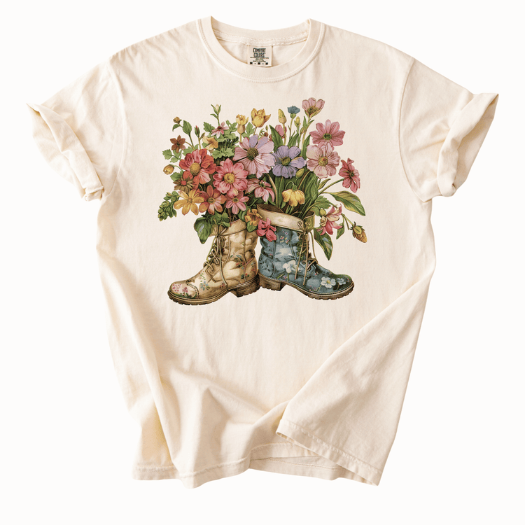 A white t-shirt with a printed design of two rain boots, one blue and one yellow, filled with colorful flowers.