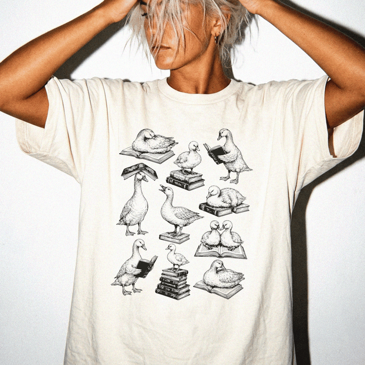 A person wearing a white t-shirt with a graphic design of various birds, including ducks, perched on books and reading.