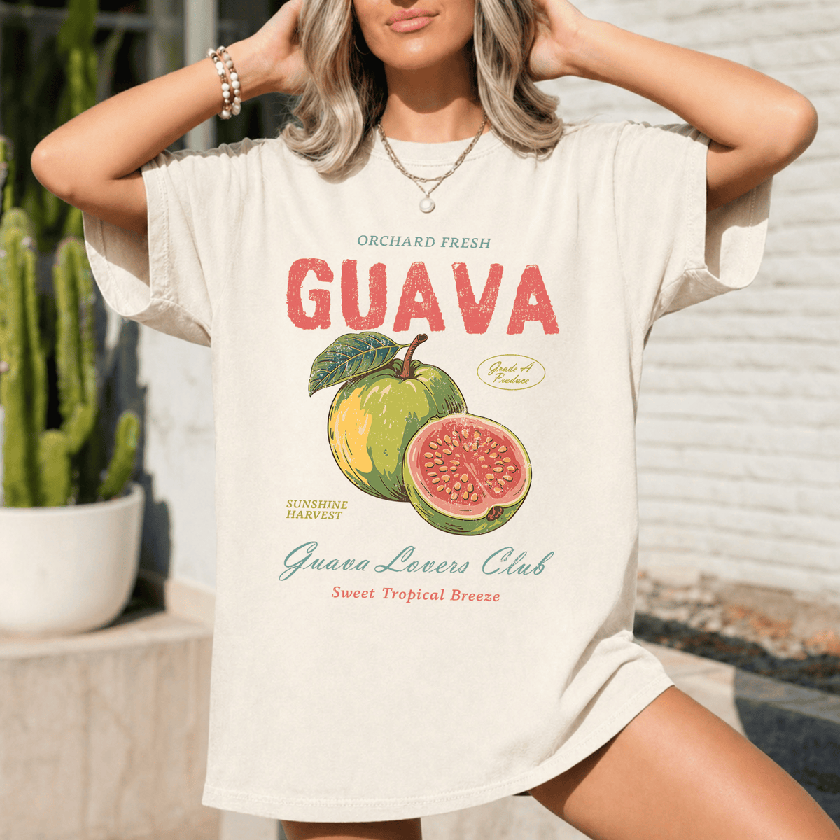 A woman wearing a white t-shirt with a graphic of a guava fruit and text that says "Orchard Fresh GUAVA" and "Guava Lovers Club Sweet Tropical Breeze".